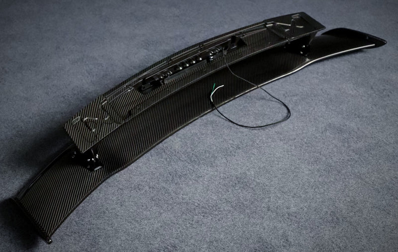 Underside view of carbon fibre rear wing showing base, mounting points and wiring