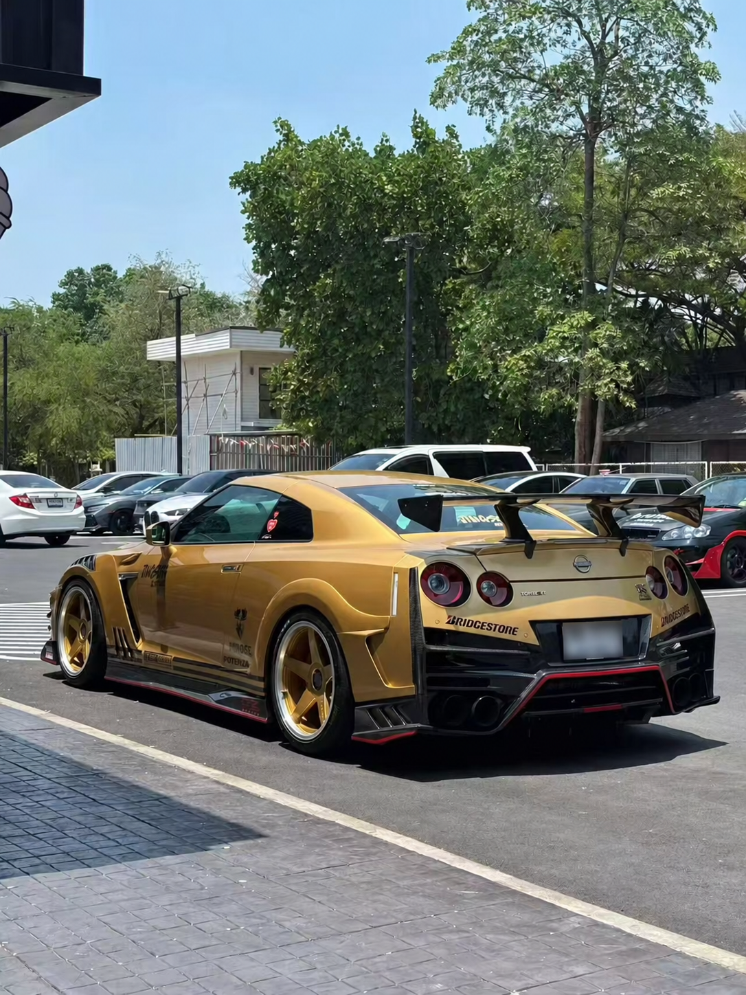Rear three-quarter reference view of a gold Nissan R35 GT-R with a Top Secret style rear spoiler; number plate blurred